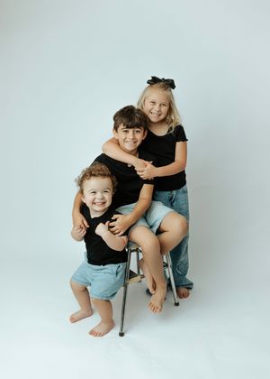 Three siblings hugging and smiling in matching black shirts during professional studio photo session.