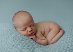 Peaceful sleeping newborn baby posed on a soft blue knit blanket in studio setting.