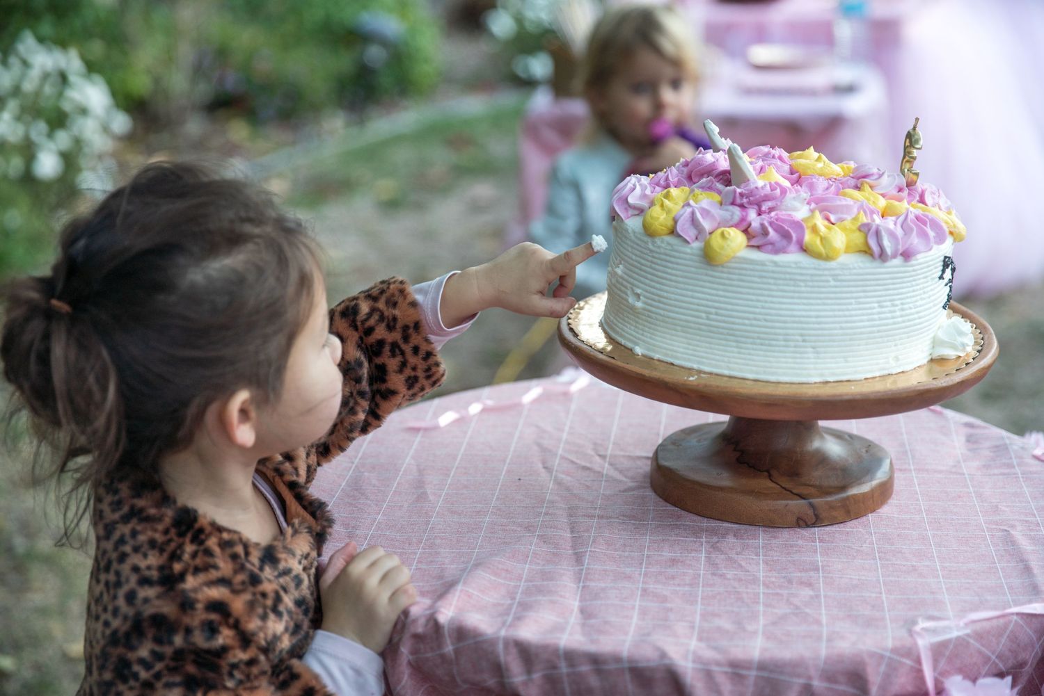 looking over the shoulder at a girl sticking her finger in her birthday cake to sneak a bite