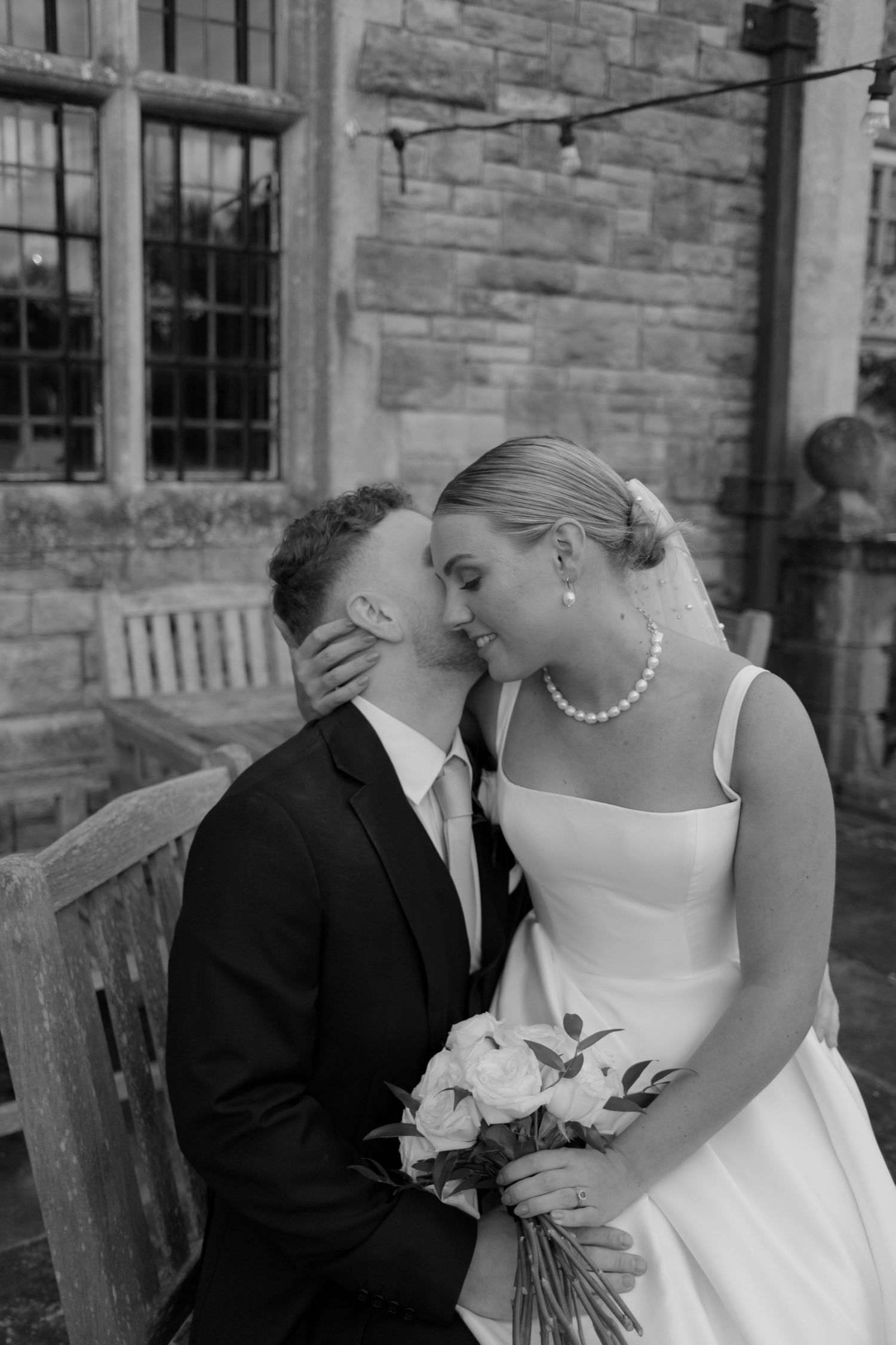 A black and white photo of a couple embracing with flowers in a tropical garden setting.