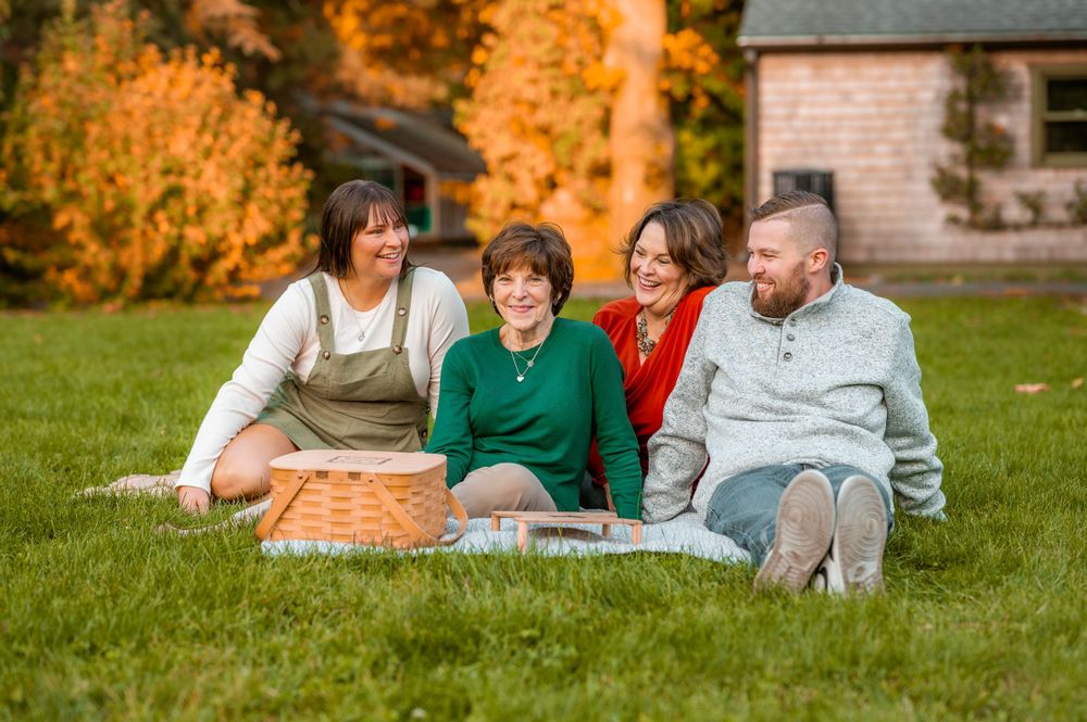 Four people lounge on an orange blanket in a grassy yard during fall.
