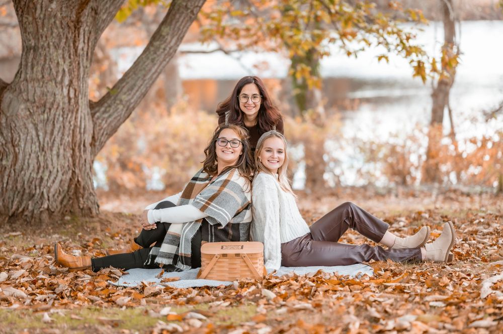 Three friends relax together on fallen leaves during an autumn photoshoot.