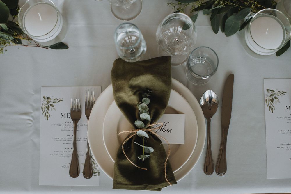 Elegant wedding place setting with white plates, brown napkin, cutlery and menu cards on a white tablecloth.