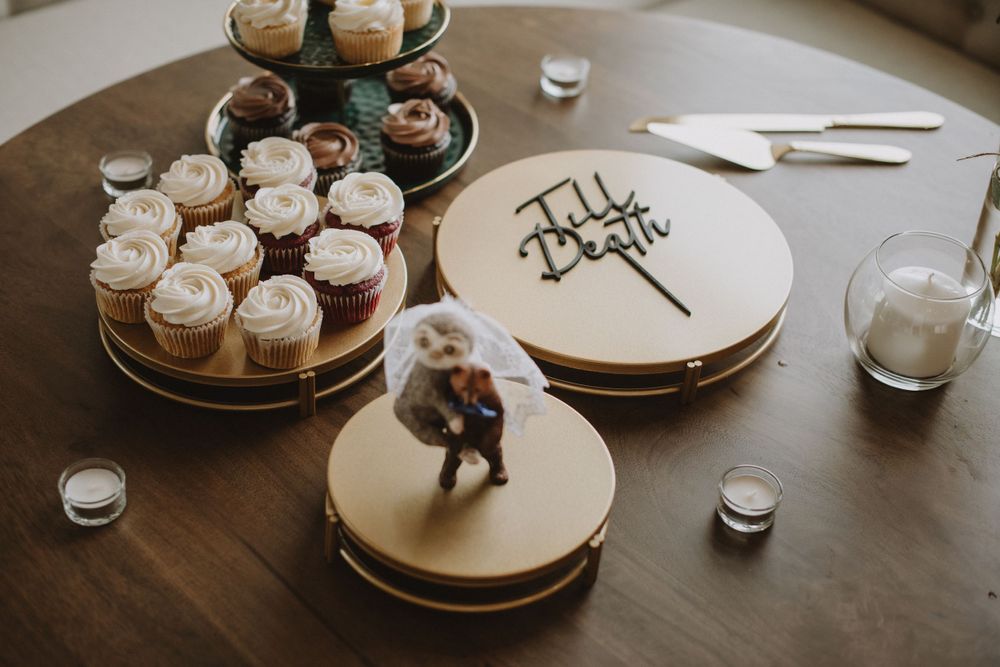 Wedding cake and cupcakes displayed on wooden stands with small decorative figures on top.