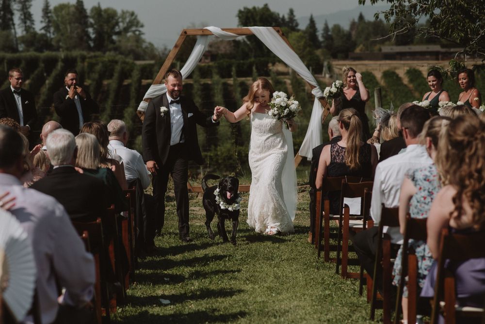 Couple celebrates their outdoor wedding ceremony while walking down the aisle under an arch in a scenic garden setting.