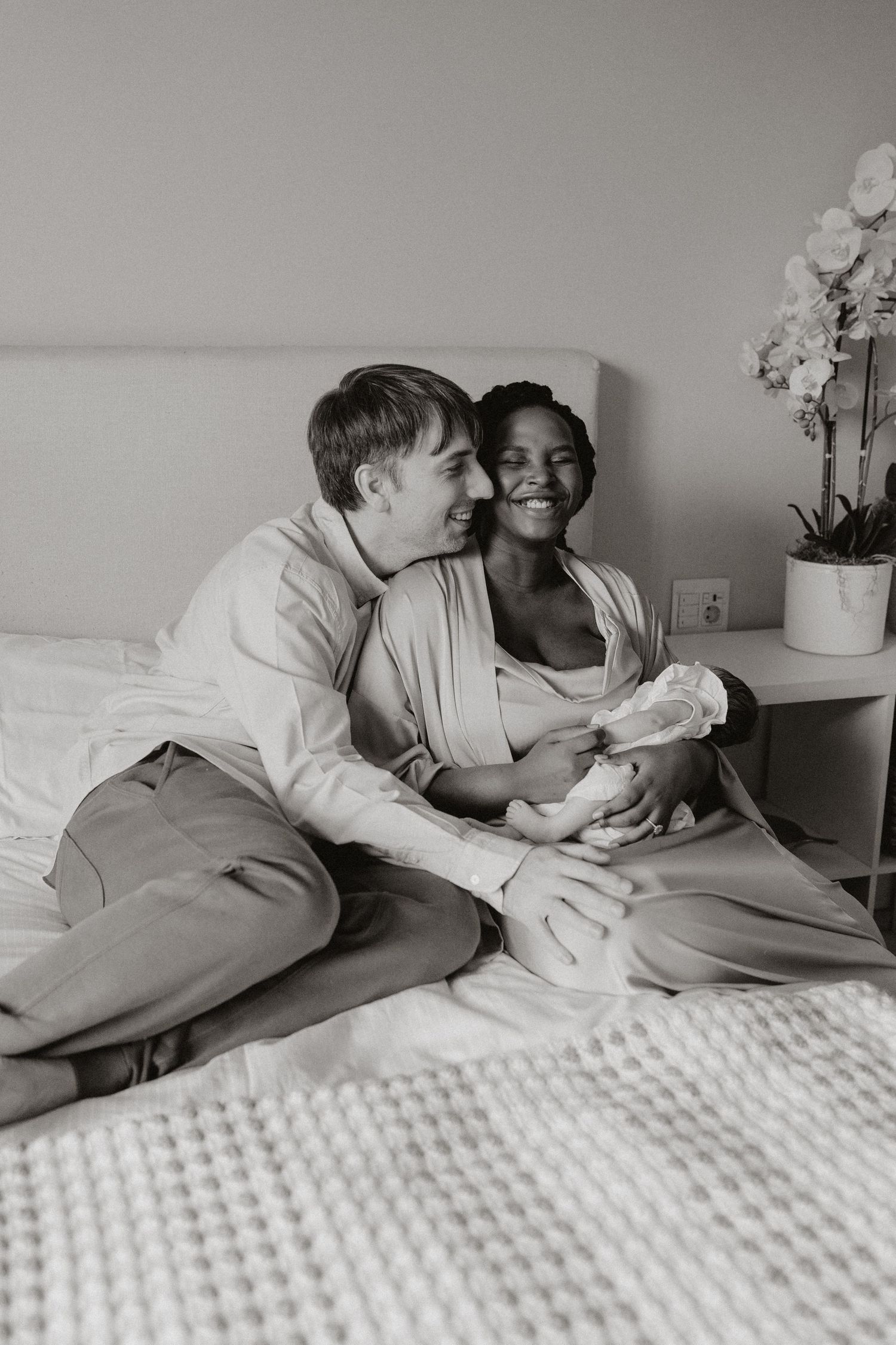 Candid moment of connection photographed on white bedding with potted orchids nearby.