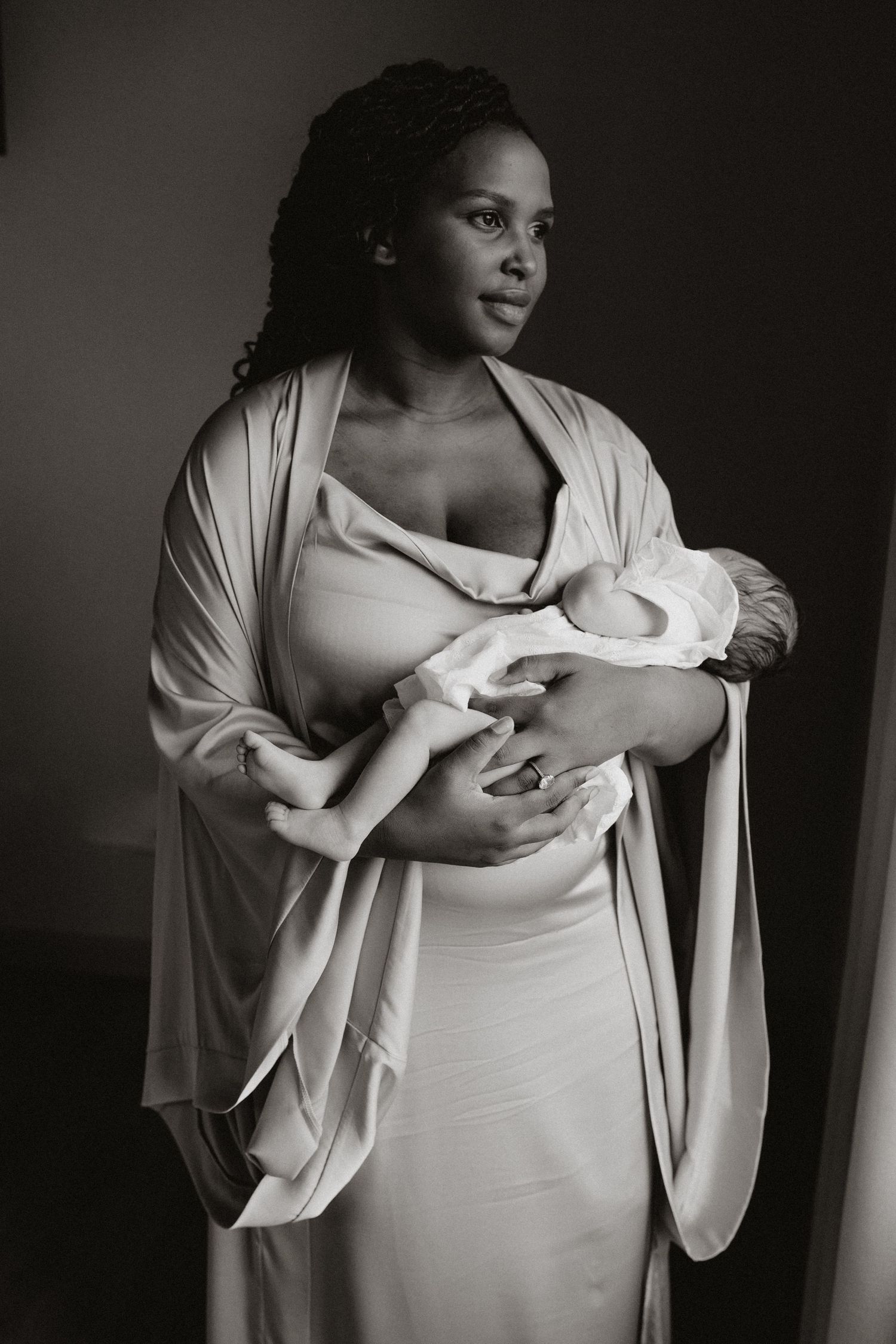 Artistic black and white portrait showing intimate maternal moment in flowing beige garments.