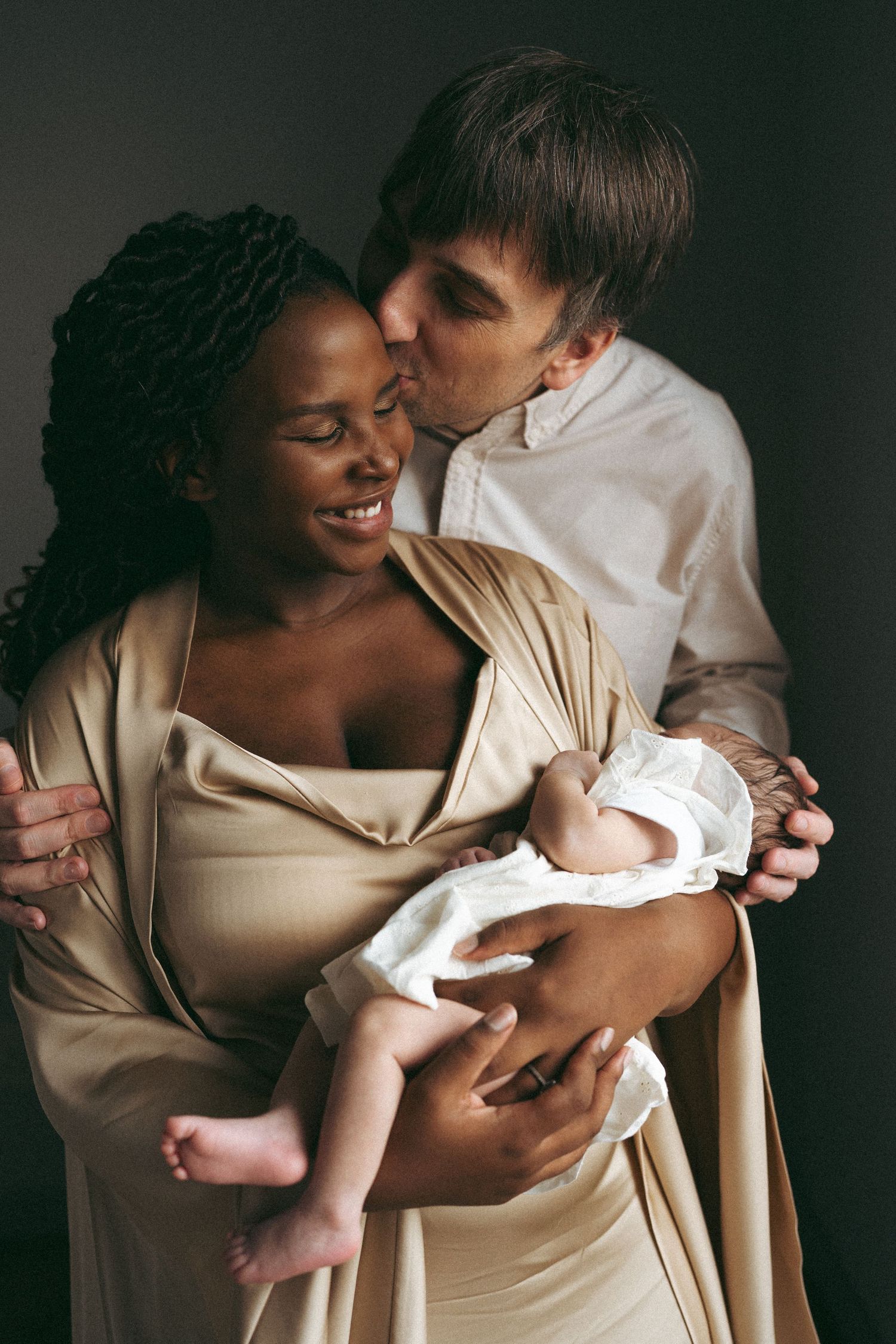 Tender family moment captured as parents share affection while holding their newborn baby.