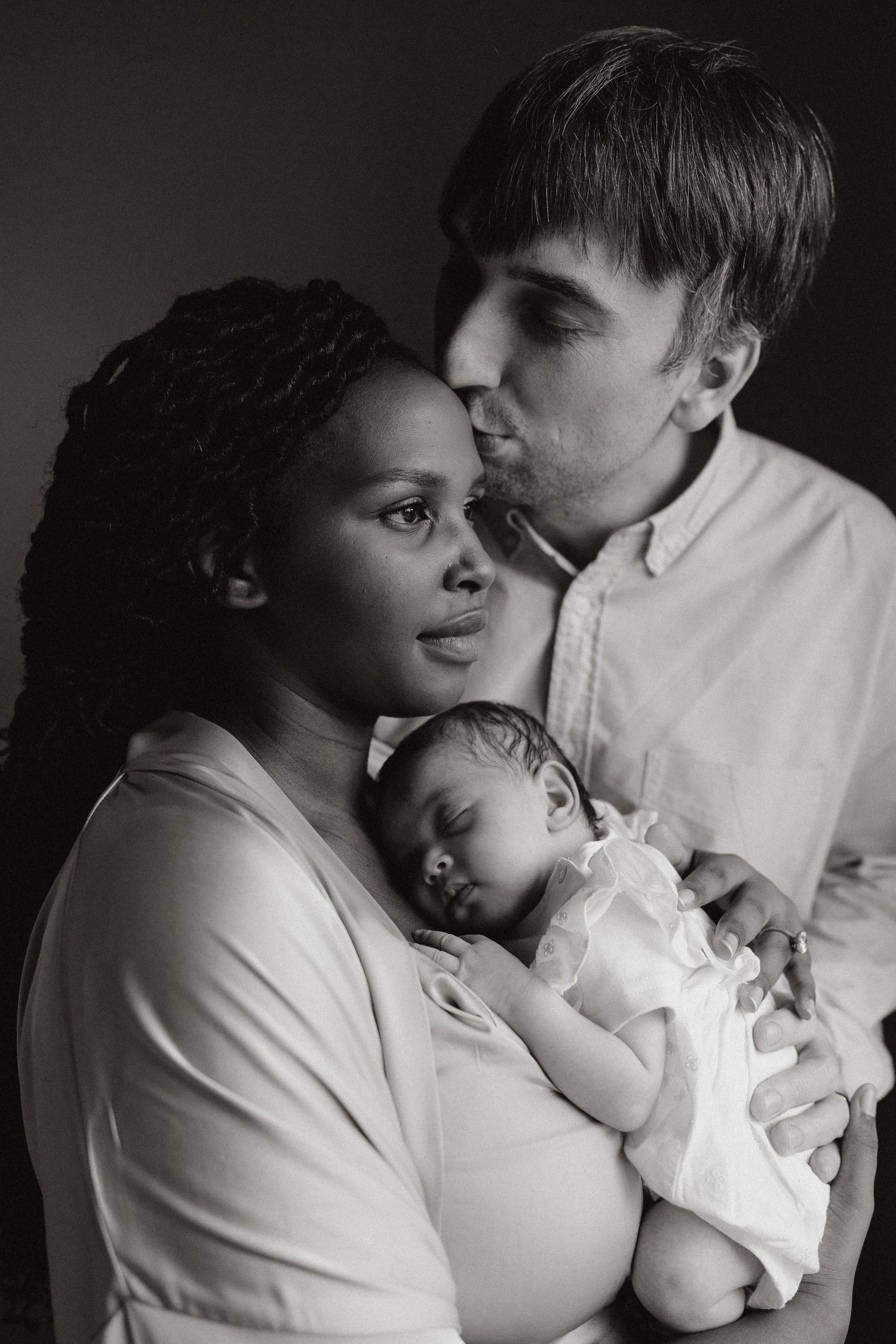 Intimate family portrait showing tender moments between parents and their newborn in monochrome.