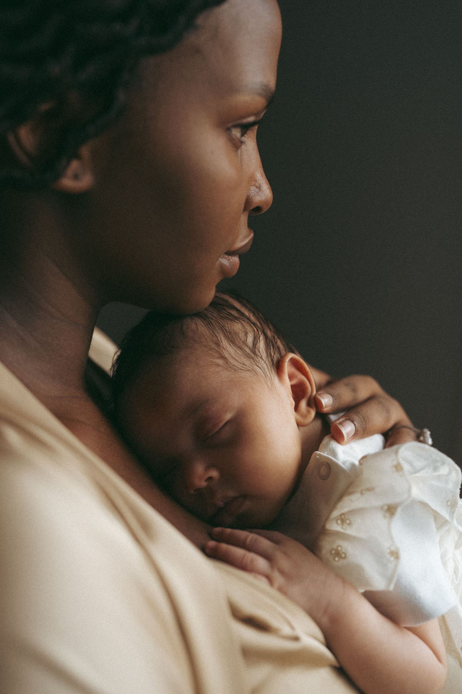 Close-up profile view of parent holding sleeping newborn baby against chest in soft lighting.