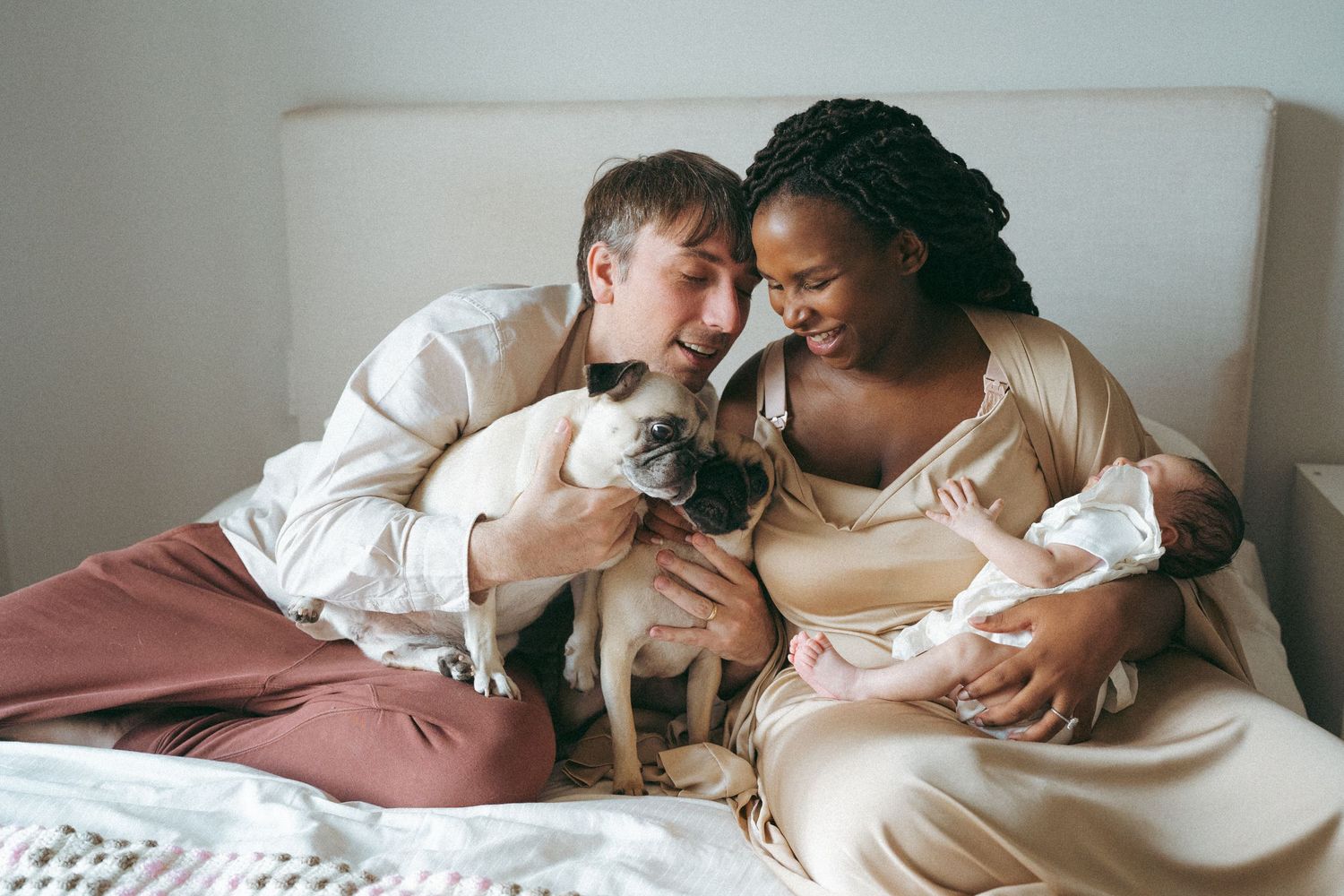 Family relaxing on couch with their pug and newborn baby in casual home setting.