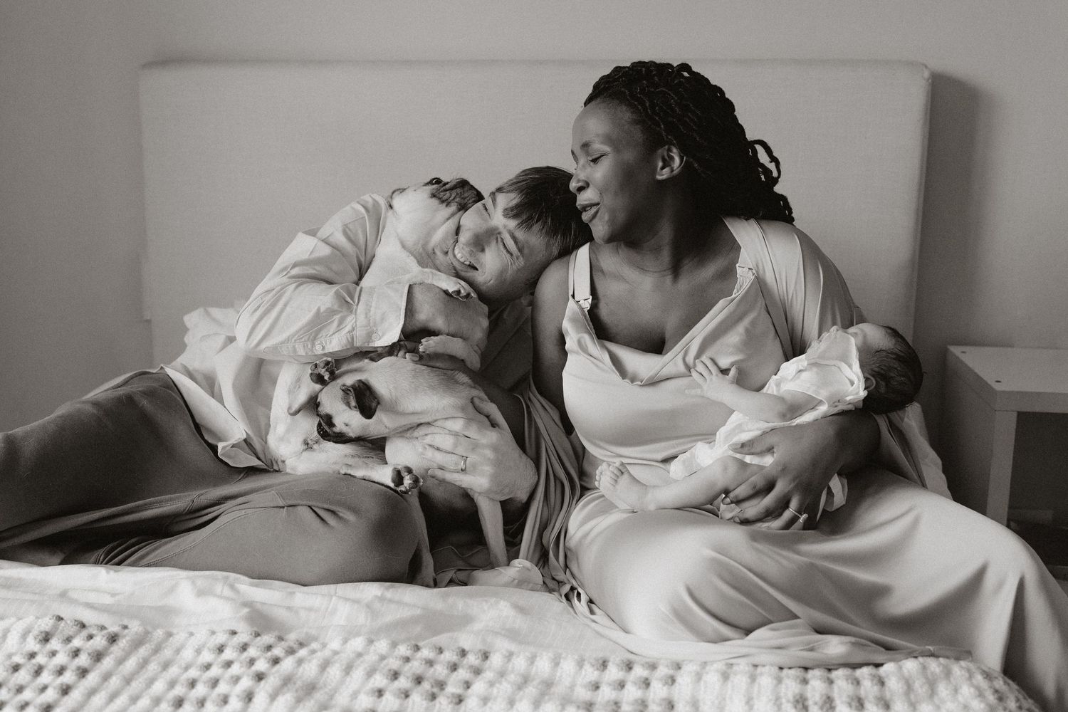 Candid moment of family laughing together with their dog and baby on white bedding.