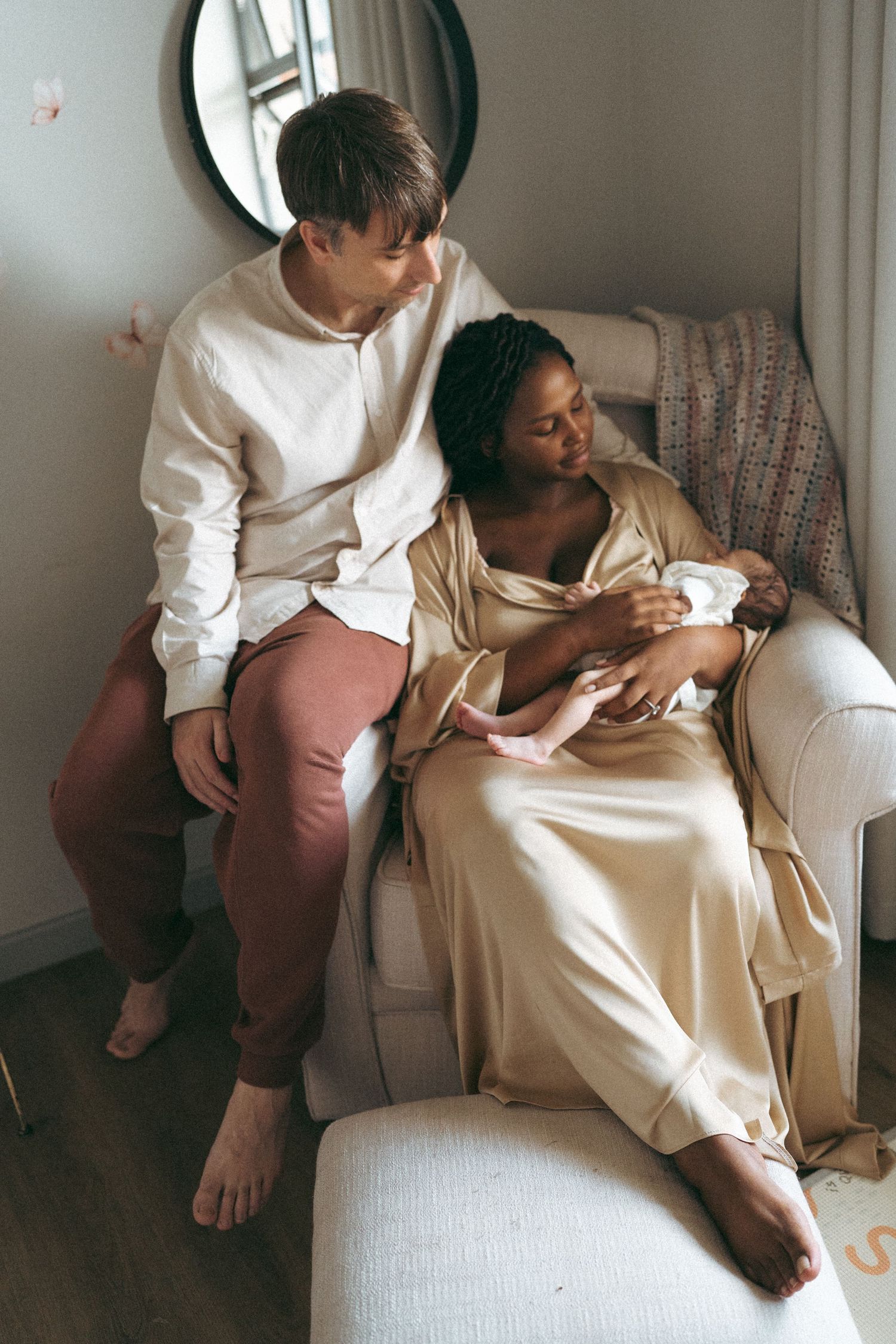 Intimate family moment on white couch as parents admire their newborn baby in natural lighting.