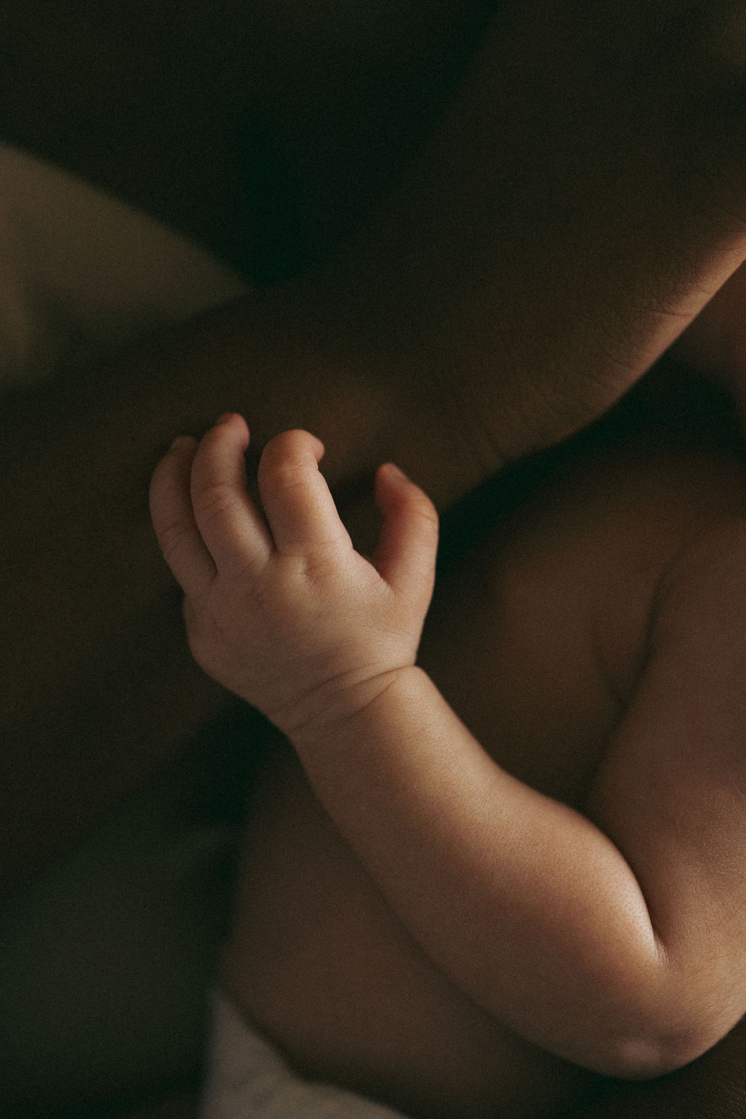 Artistic close-up of a baby's arm and hand in moody lighting.