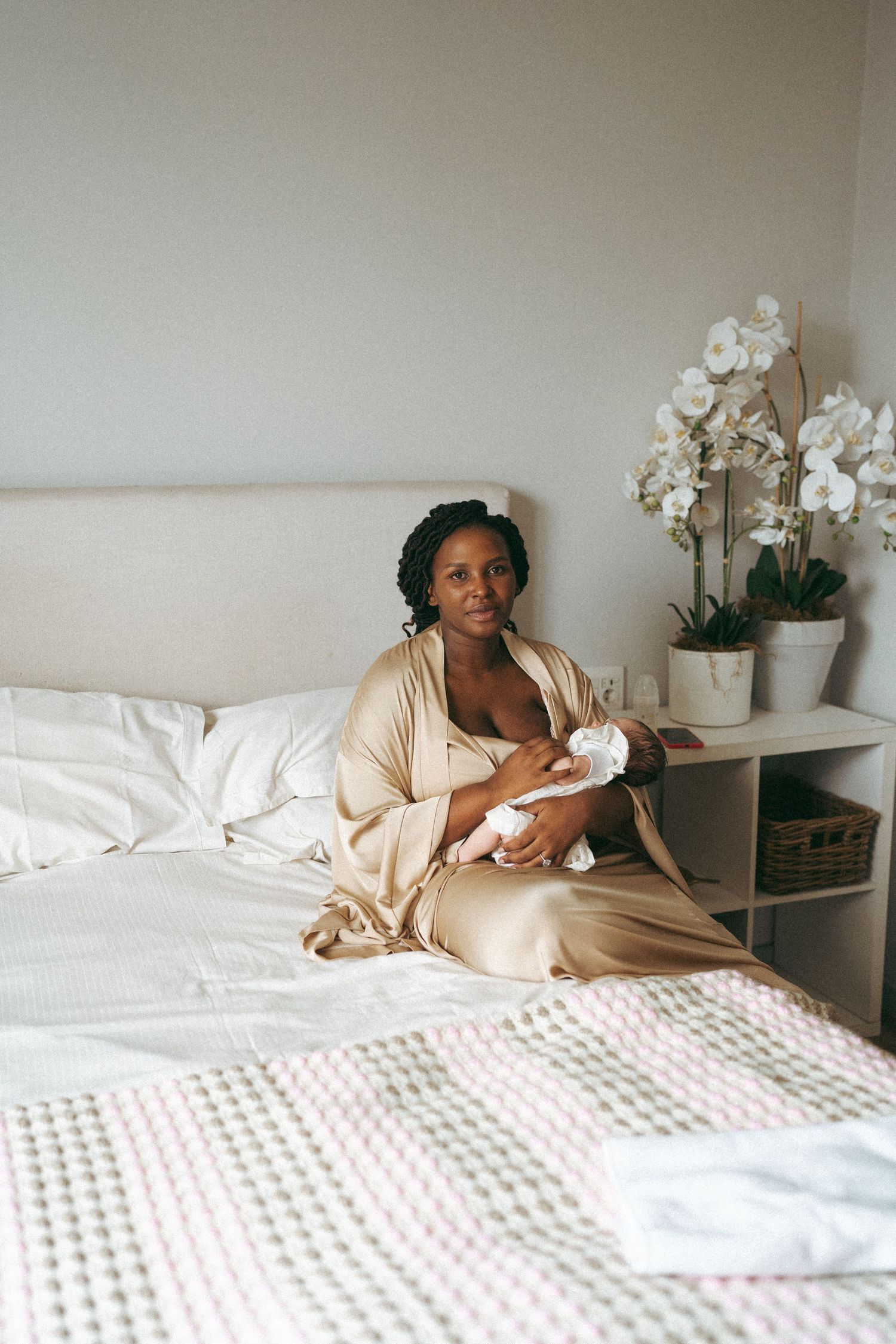Woman relaxing on white bedding with orchids in a bright, minimalist bedroom setting.
