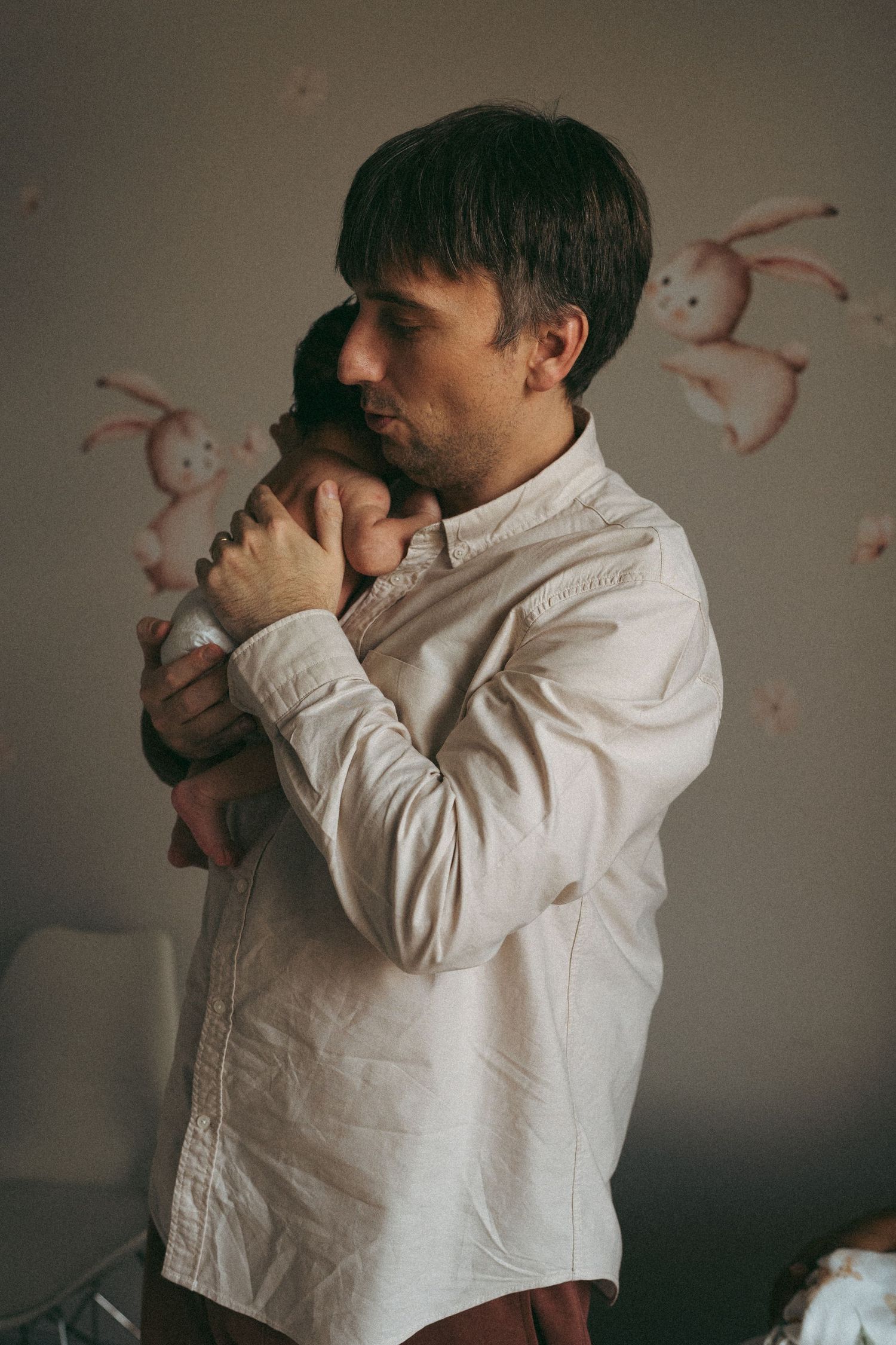 Parent in white shirt holding infant against wall with pink bunny decorations.