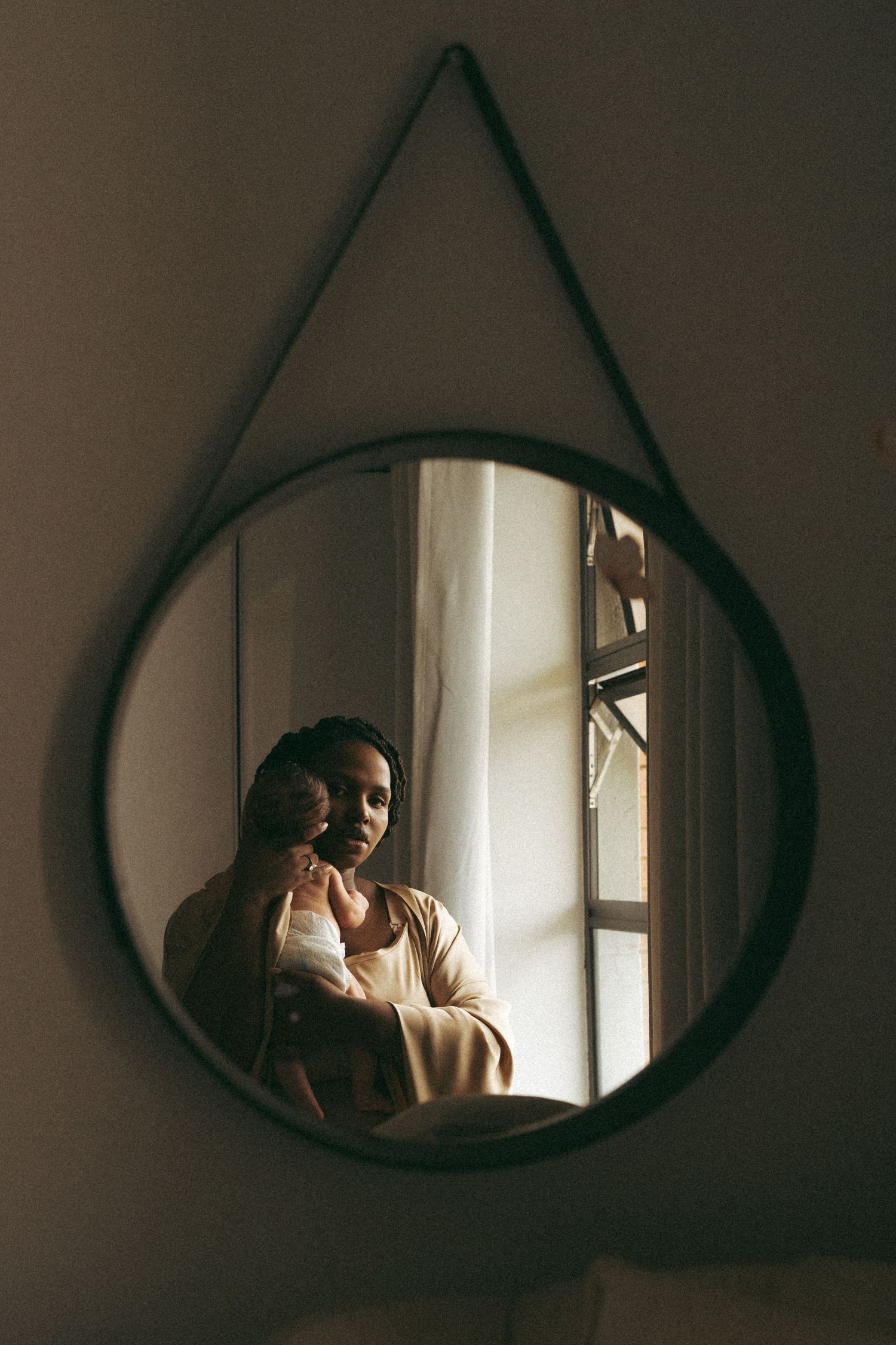 Reflection in round mirror shows parent holding baby near window in natural light.