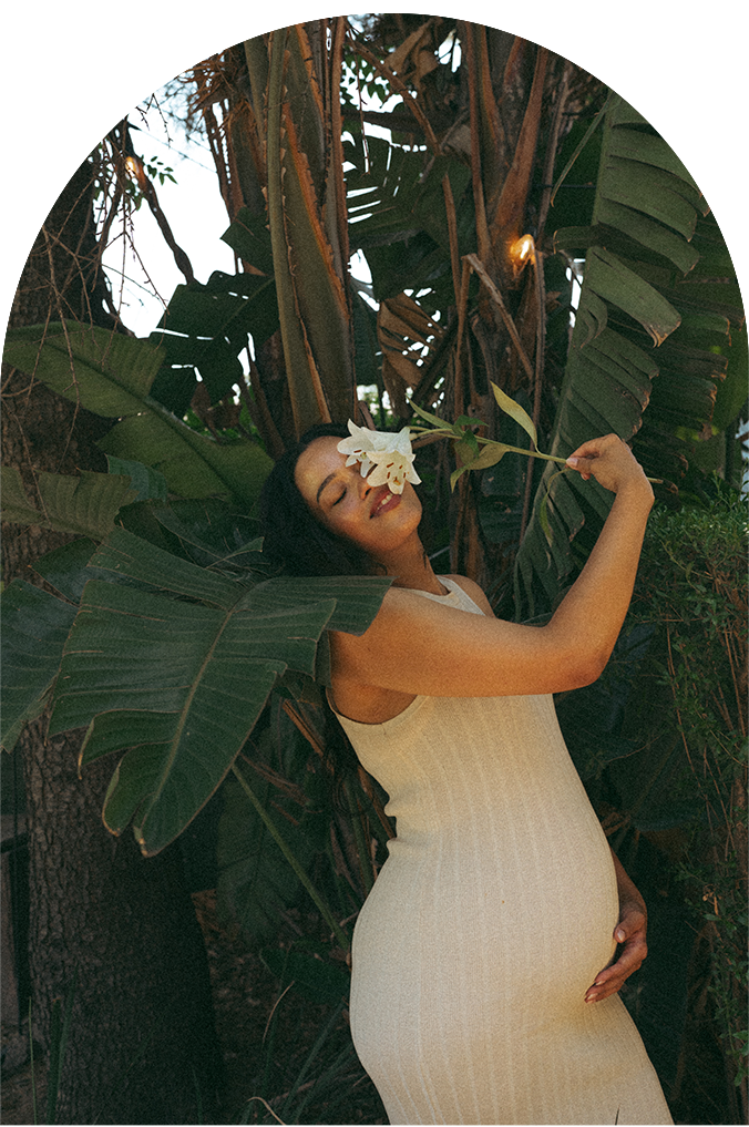 Person in white dress poses against tropical foliage in arched photo series.