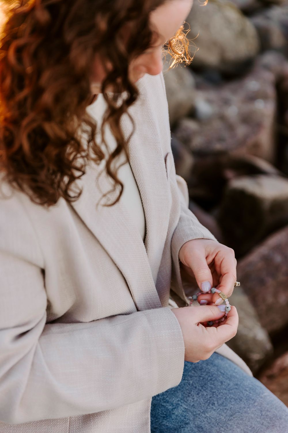 Detaljebillede af krøllet hår og cremefarvet blazer mod en tekstureret stenvæg. Branding fotograf Fyn.