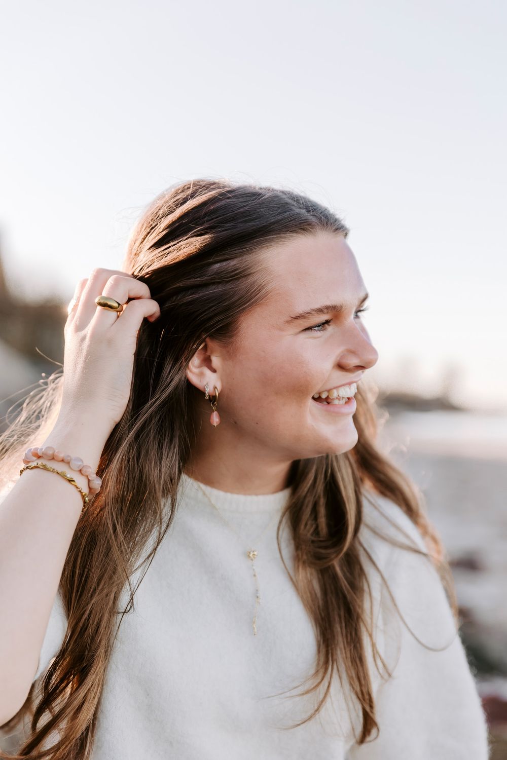 Person i cremefarvet sweater smiler og leger med håret. Branding fotograf Fyn.