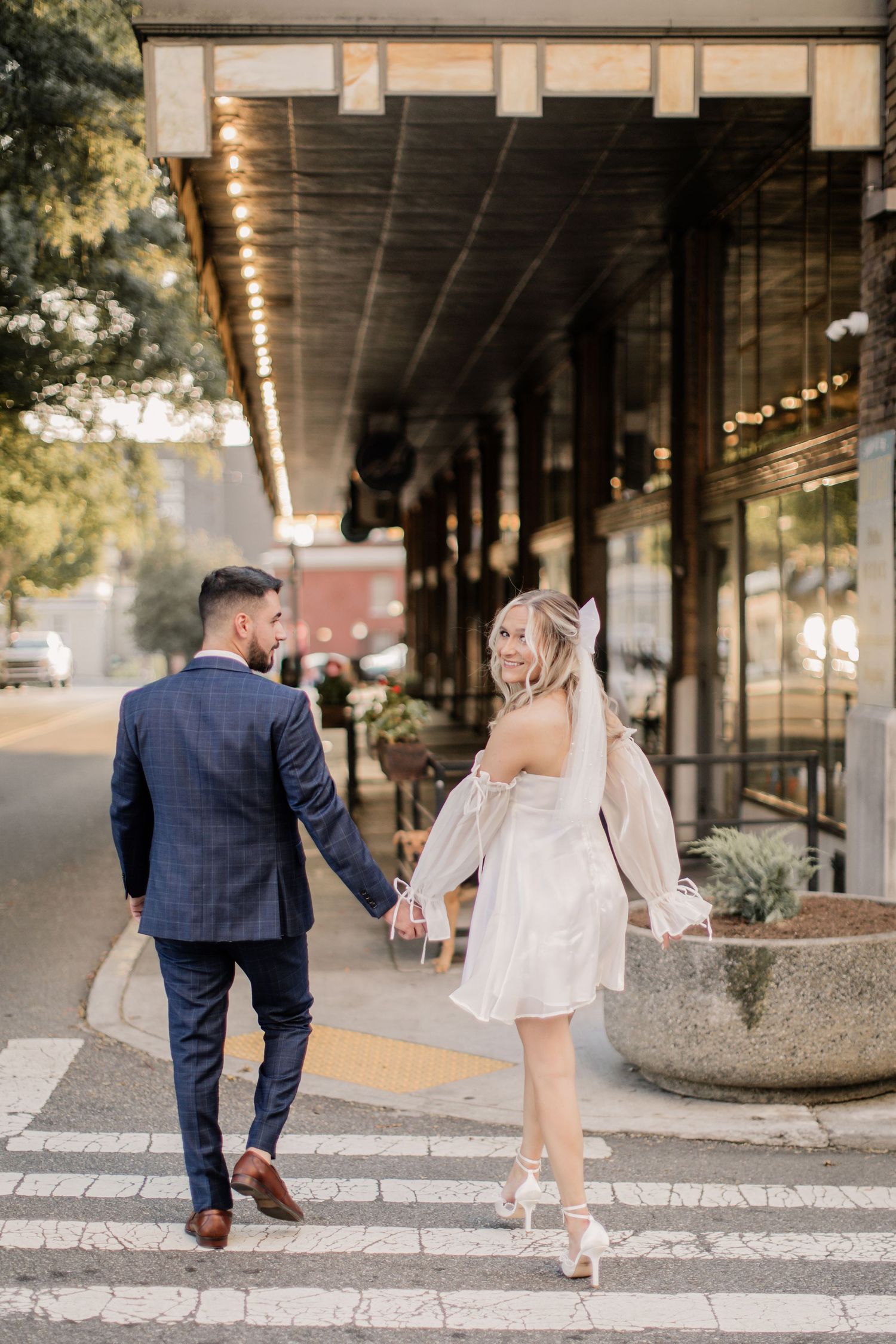 A couple in wedding attire playfully walks and poses along a covered urban walkway in a romantic photo sequence.