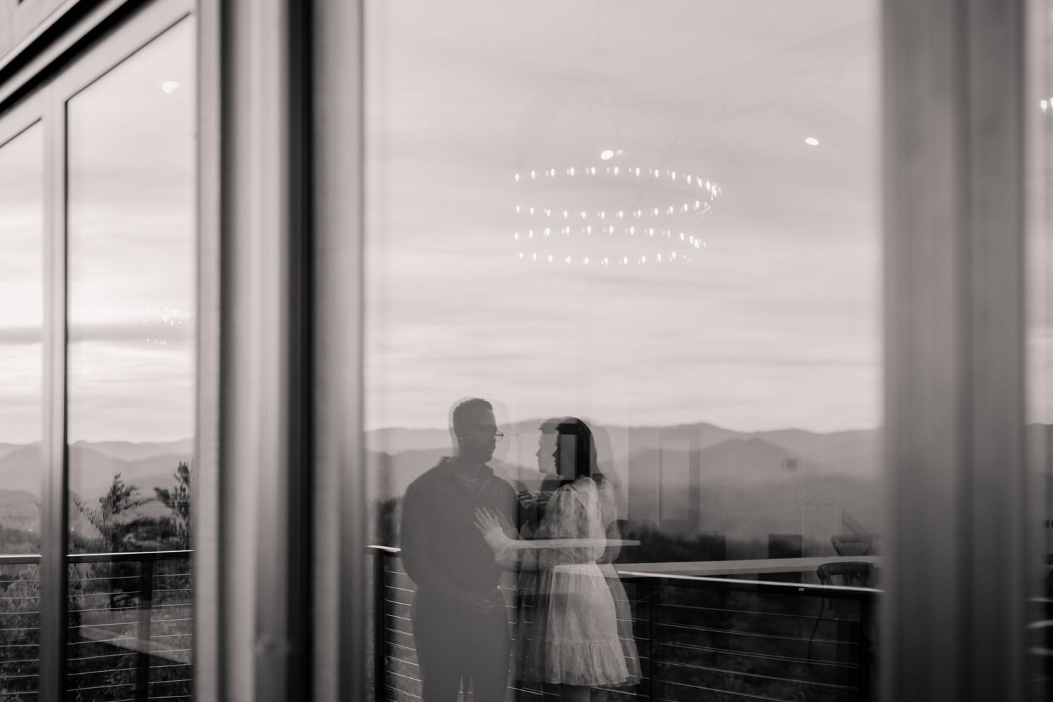 A panoramic black and white view through glass windows showing silhouettes against a distant mountain landscape.