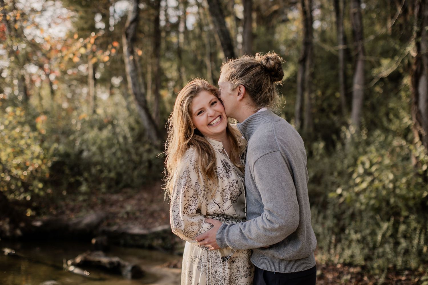 A couple shares intimate moments in a sunlit autumn forest setting during a romantic photoshoot.