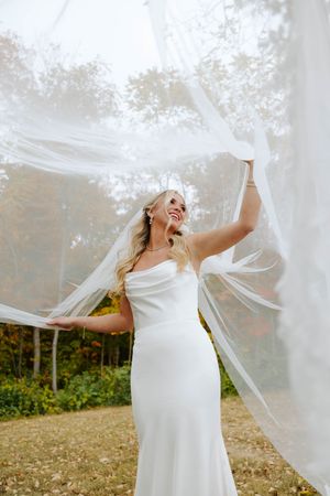 A bride in a white dress twirls joyfully outdoors with her veil flowing in the autumn breeze.