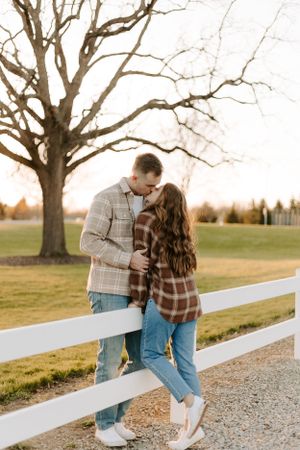 Couple in plaid sharing intimate moment by white fence during sunset.