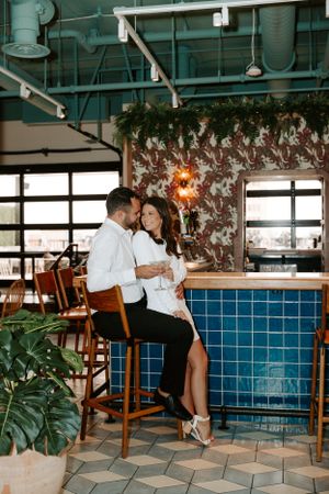 Couple shares intimate moment at modern bar with blue tile and hanging greenery.