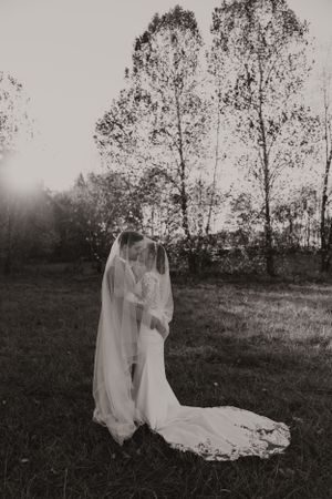 Black and white wedding photo of a couple embracing in a misty field with tall trees.