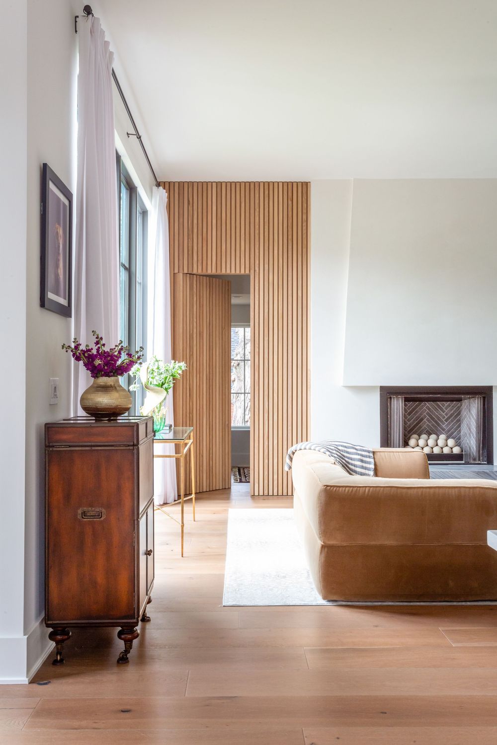 Modern minimalist interior with wooden floors and white walls featuring scattered furniture pieces.