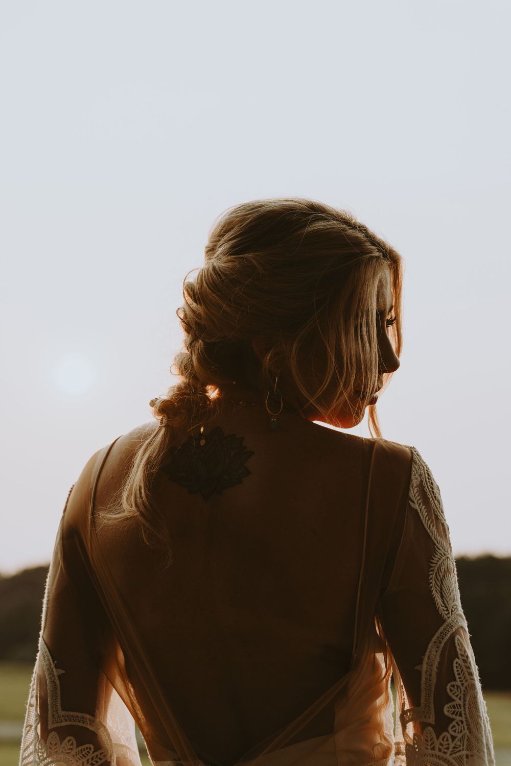 Artistic backlit portrait of a bride in a lace dress at golden hour with soft lighting.