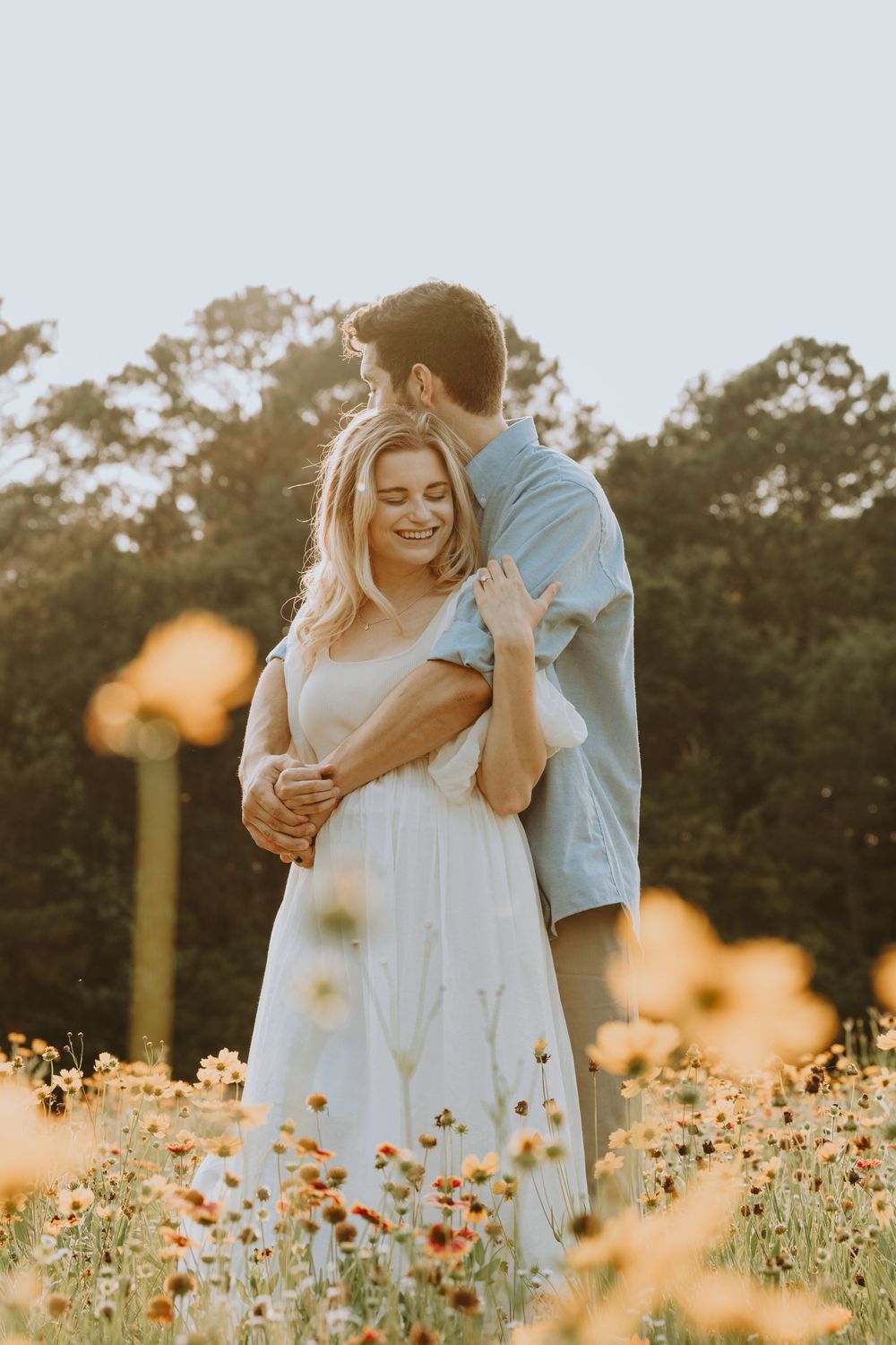 Romantic couple embracing in a field of yellow wildflowers during golden hour.