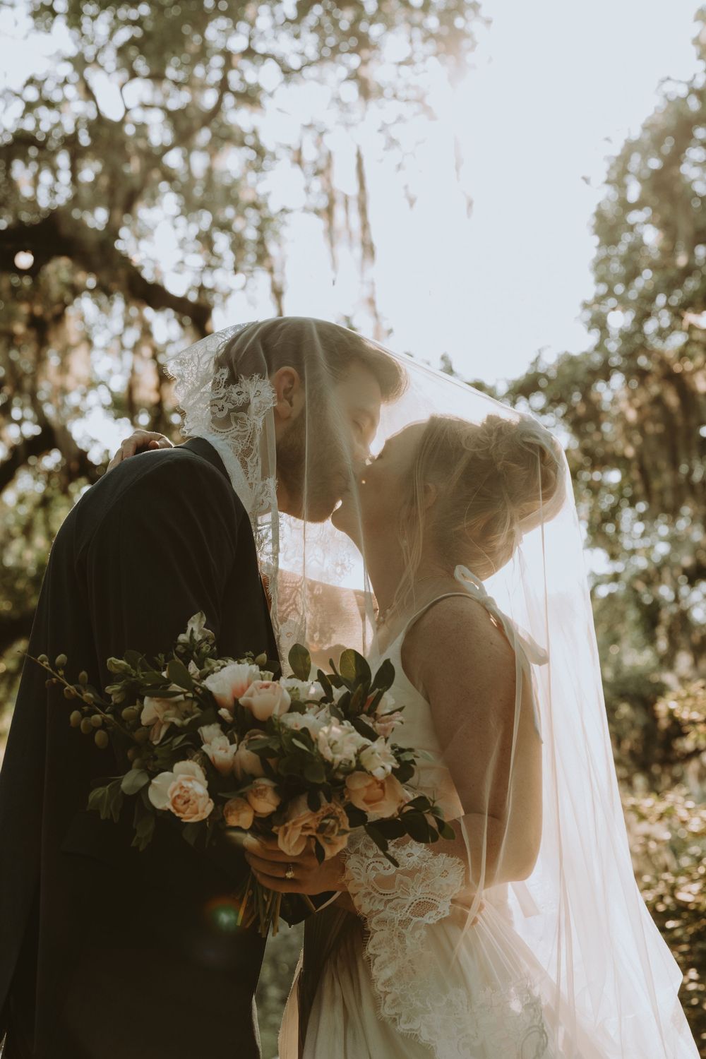 Newlyweds share an intimate moment under a veil with a bouquet of white roses.