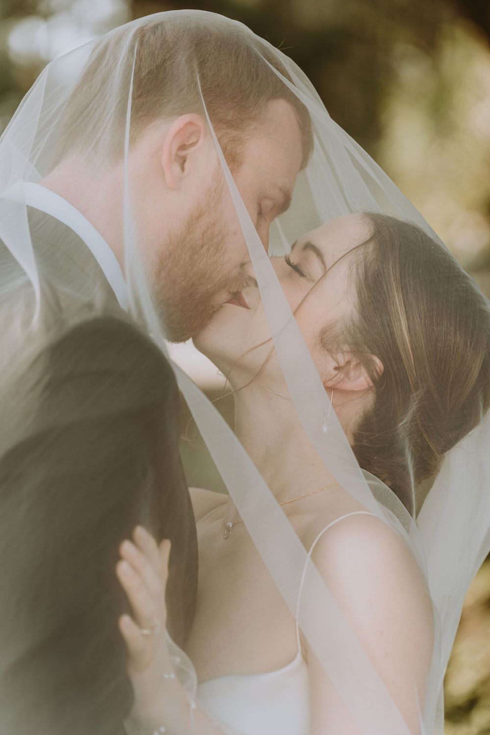 Intimate wedding portrait through sheer veil with soft natural lighting.