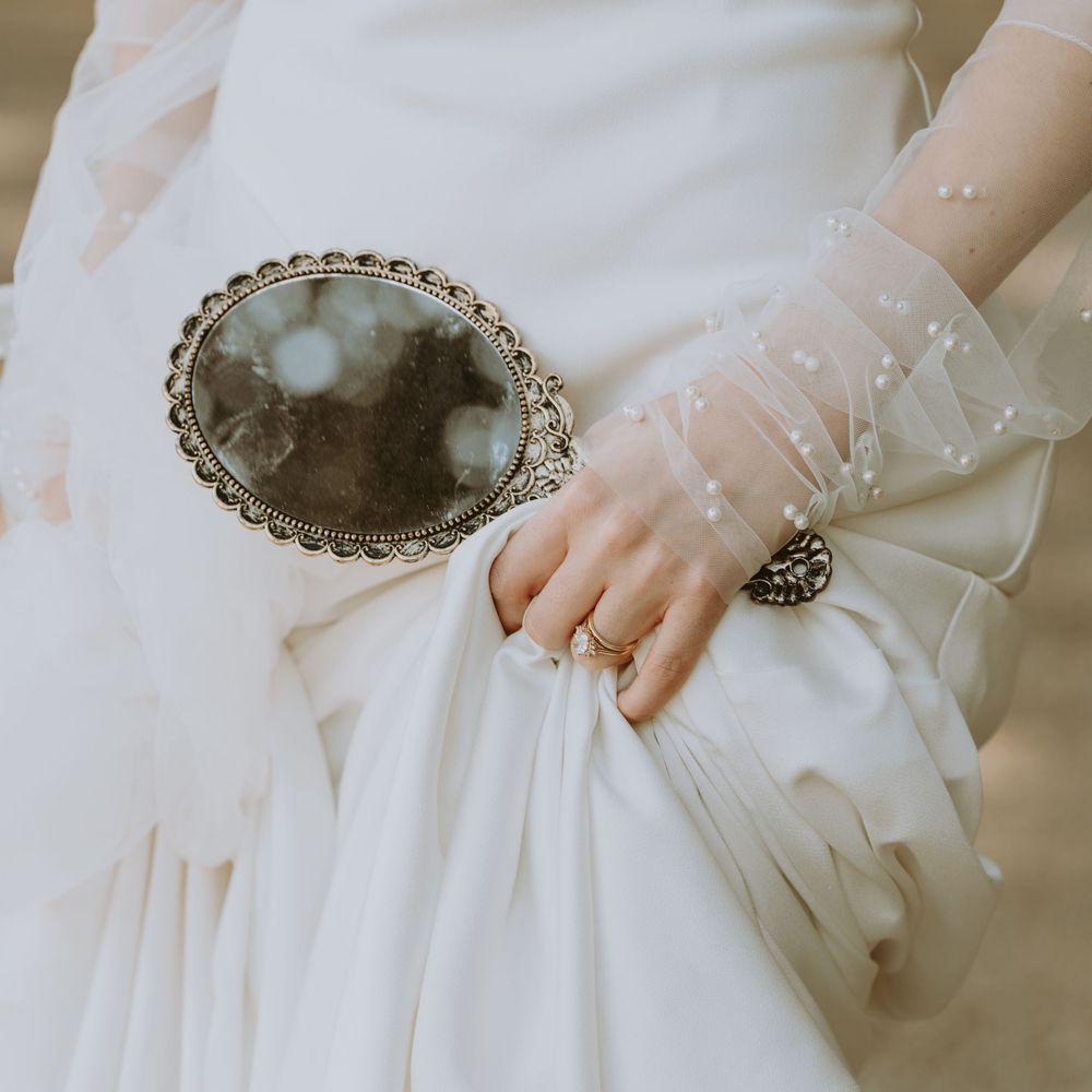 Close-up detail of vintage mirror and delicate lace sleeve on wedding dress.