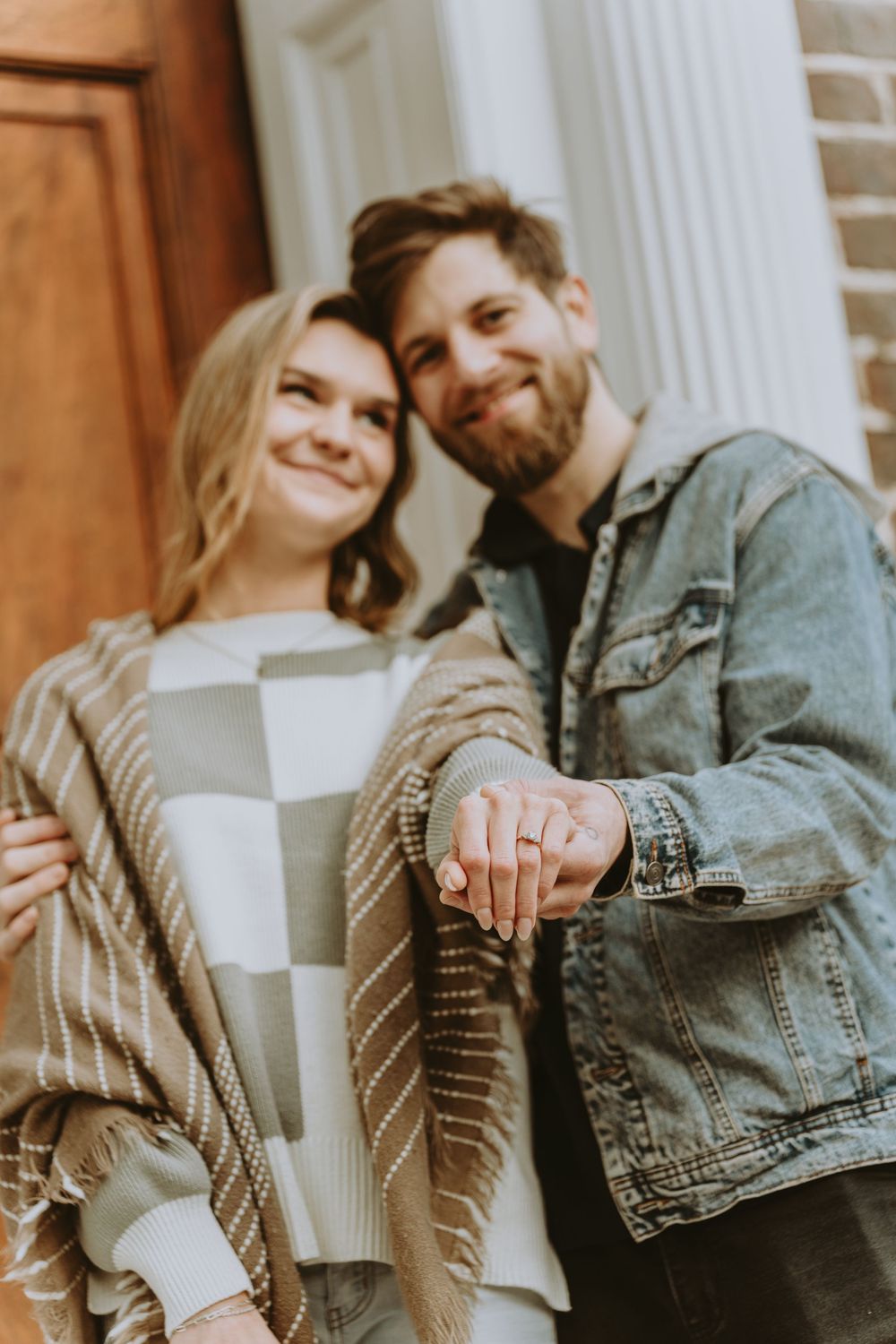 Couple showing engagement ring in romantic outdoor setting with white columns.