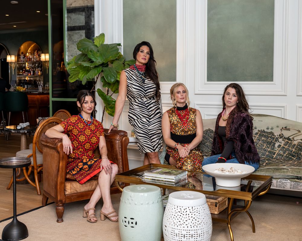Group of women in colorful dresses lounging on vintage furniture in an elegant room.