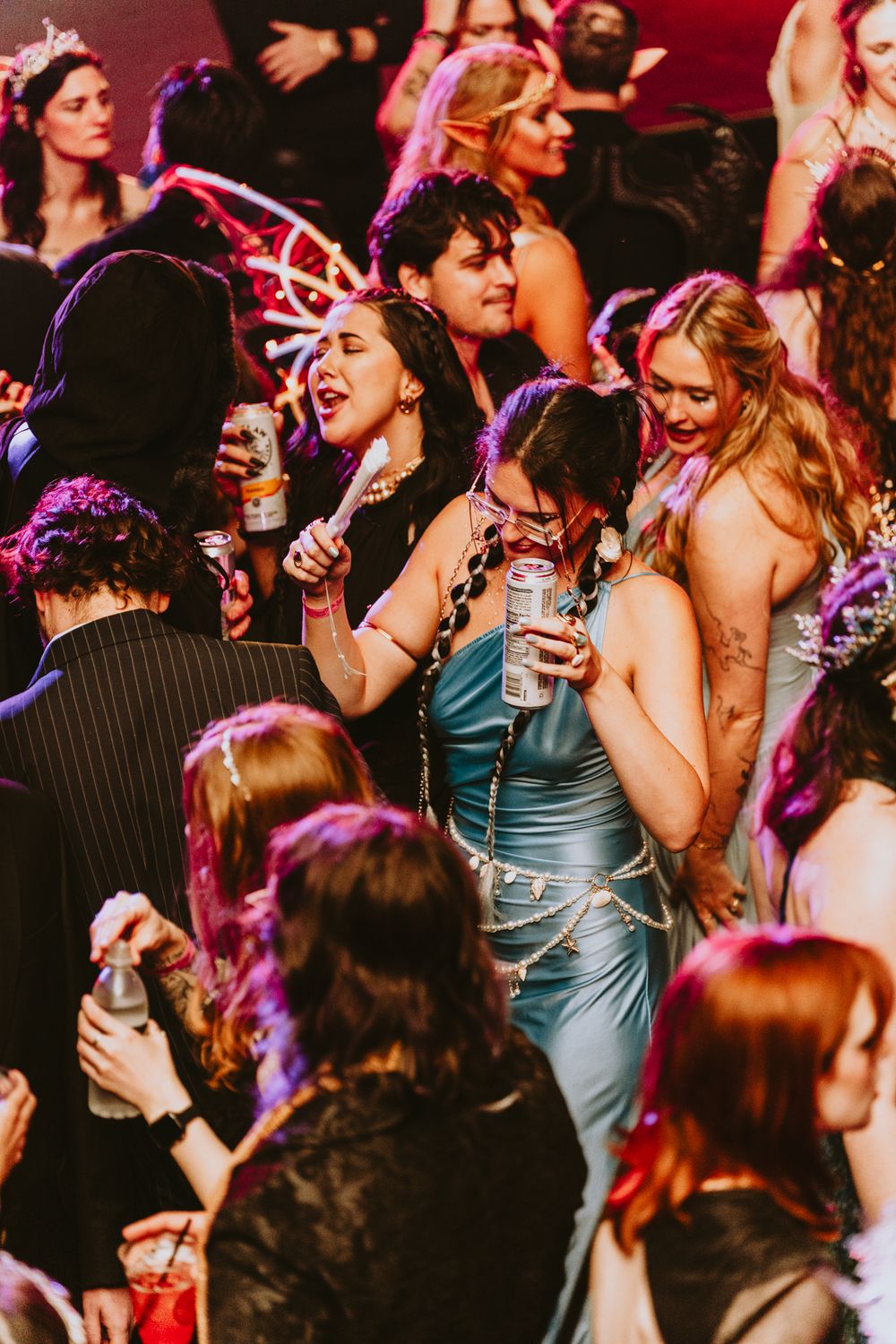 Crowded dance floor with party-goers dancing under purple and pink lighting.