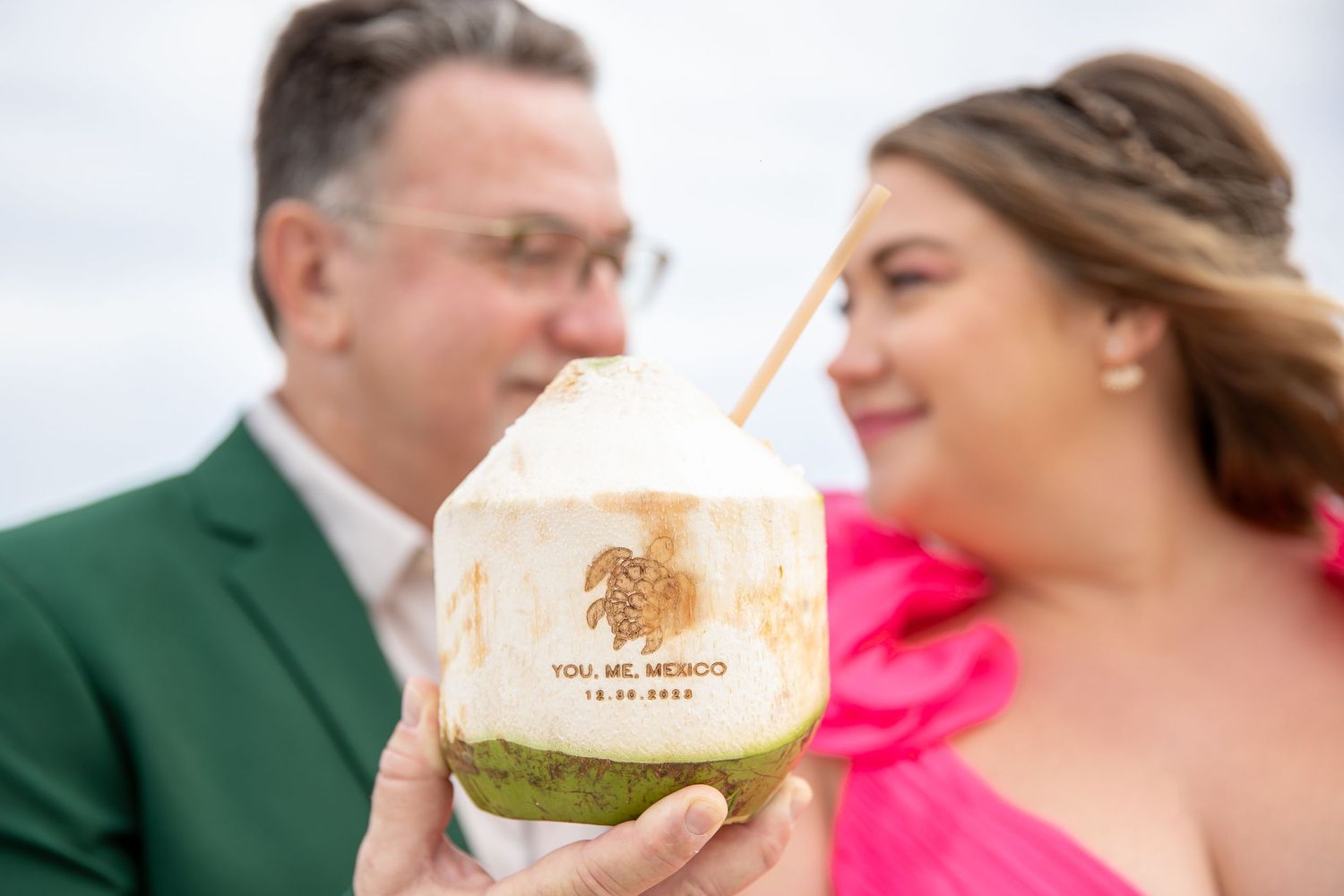 A tropical drink in a coconut is held up against an ocean backdrop.