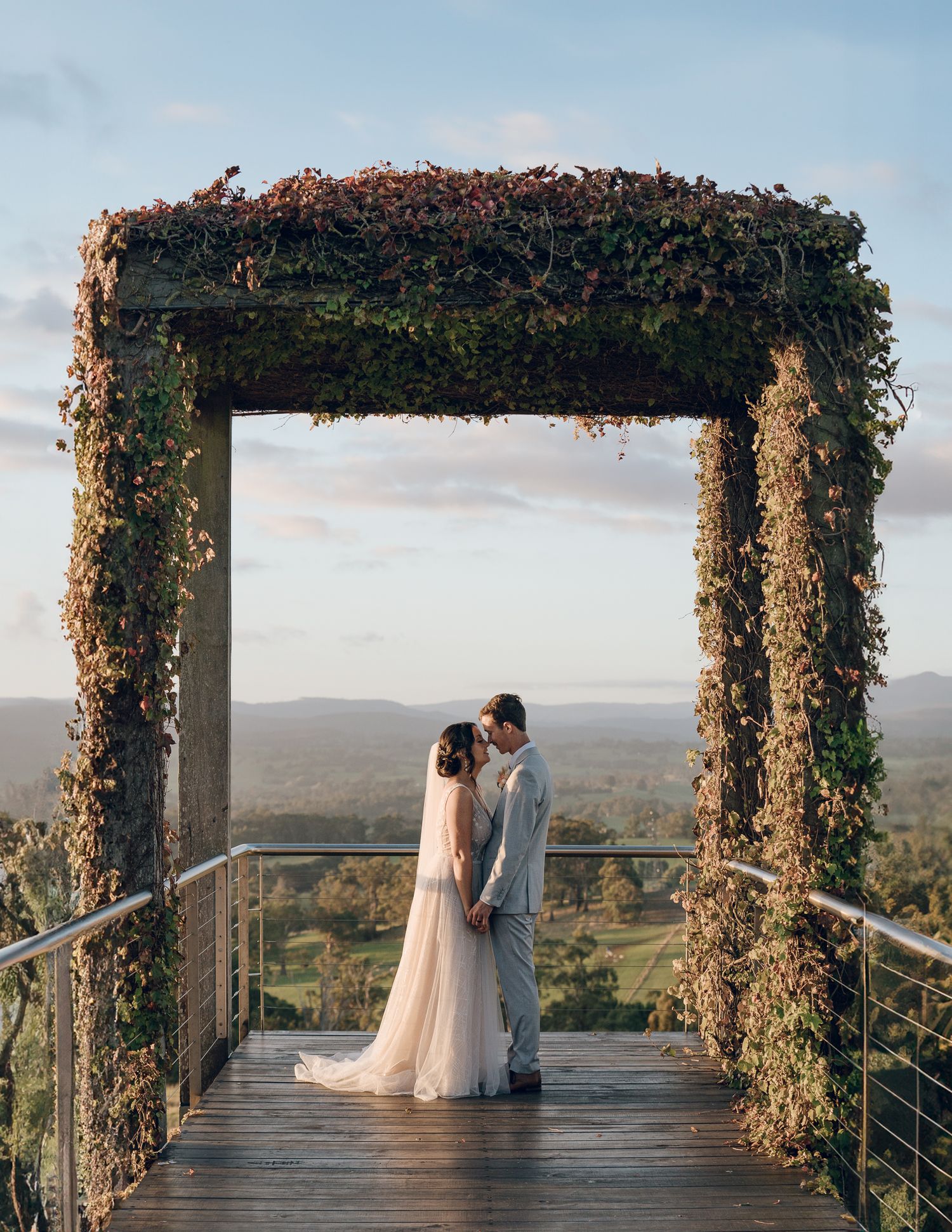 Romantic couple sharing intimate moment on vine-covered wooden deck overlooking mountain vista.