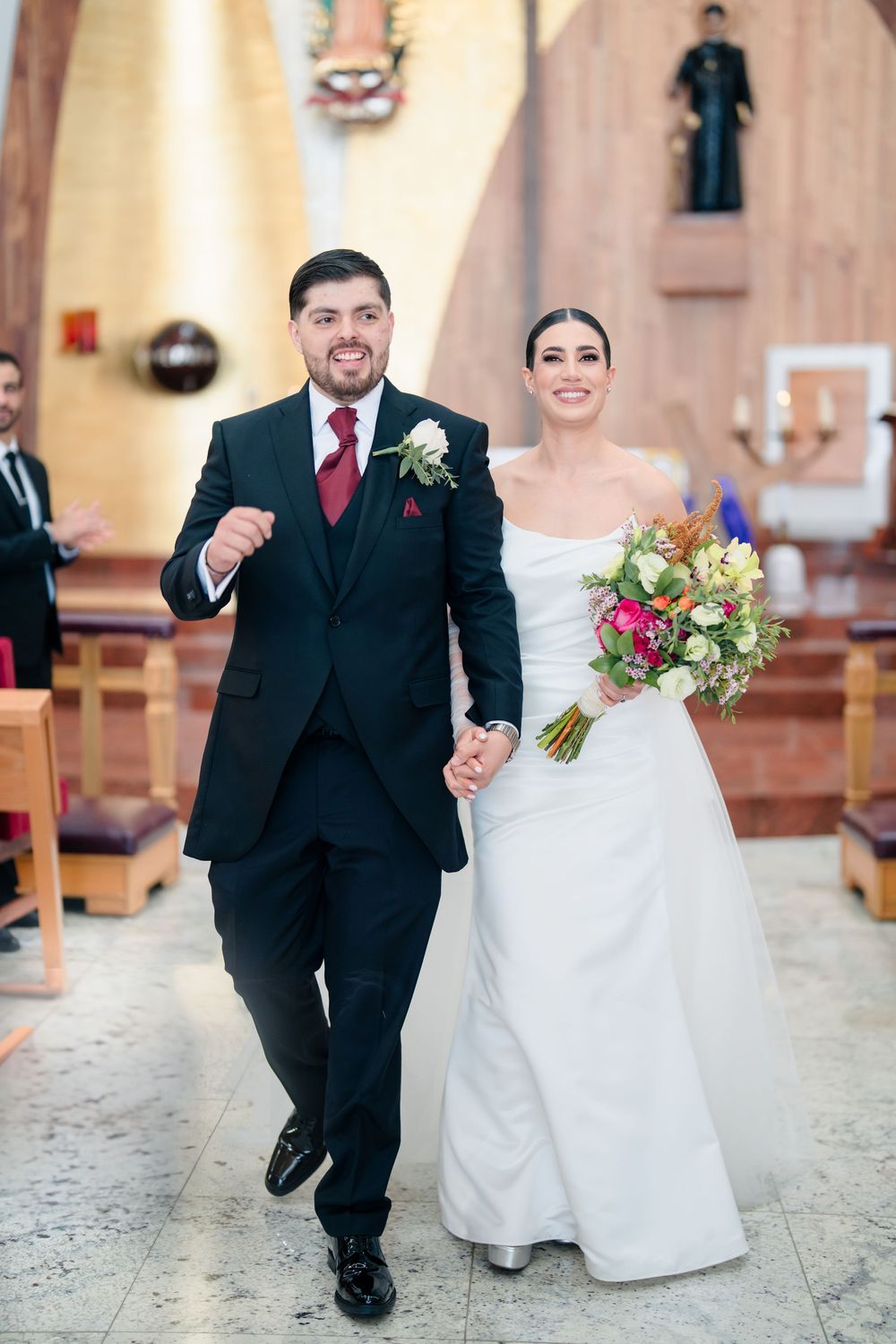 Joyful wedding couple walking down church aisle in classic black and white attire.