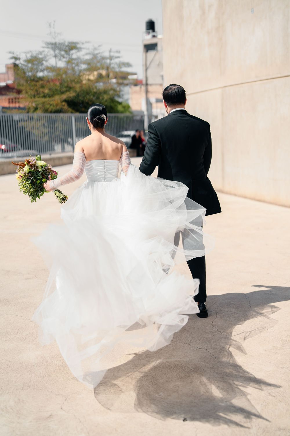 Dynamic wedding couple running through outdoor courtyard with flowing white dress.