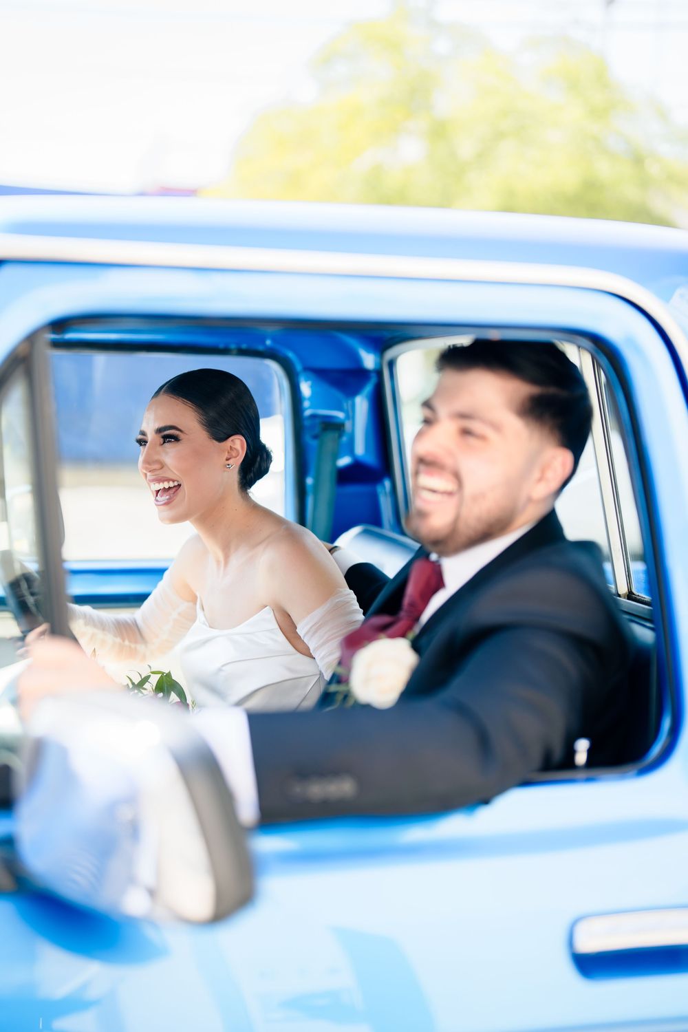 Happy newlyweds sharing laughter while riding in classic blue vintage car.