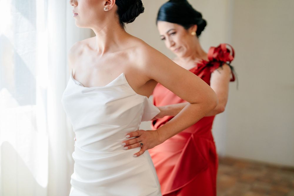 Bride in white strapless gown with bridesmaids in coral dresses during wedding preparations.
