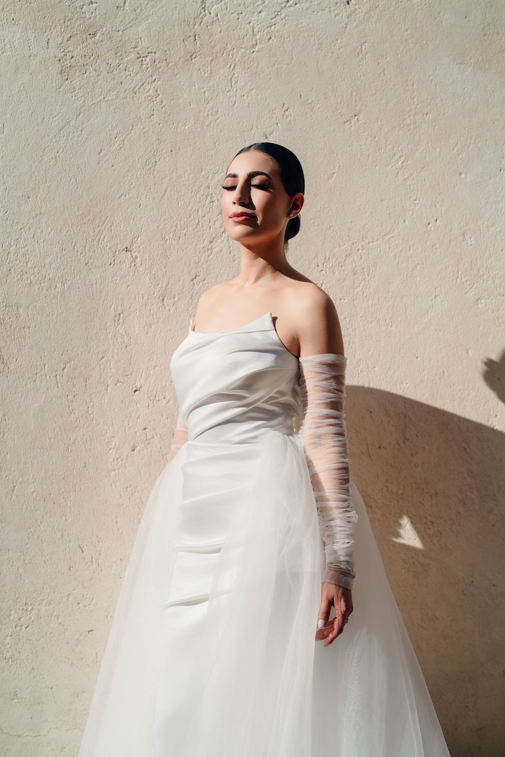 Bridal portrait series showing flowing white gown with sheer long sleeves in soft lighting.