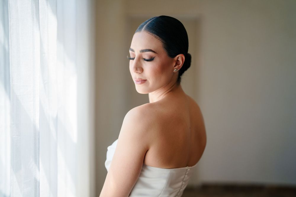 Serene bridal portrait near a sunlit window showcasing an elegant updo and strapless gown.