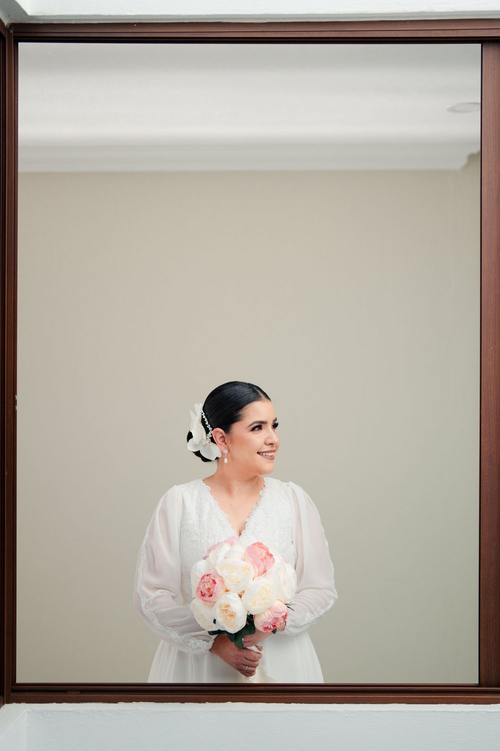 Person in white dress holding pink and white bouquet against neutral wall.
