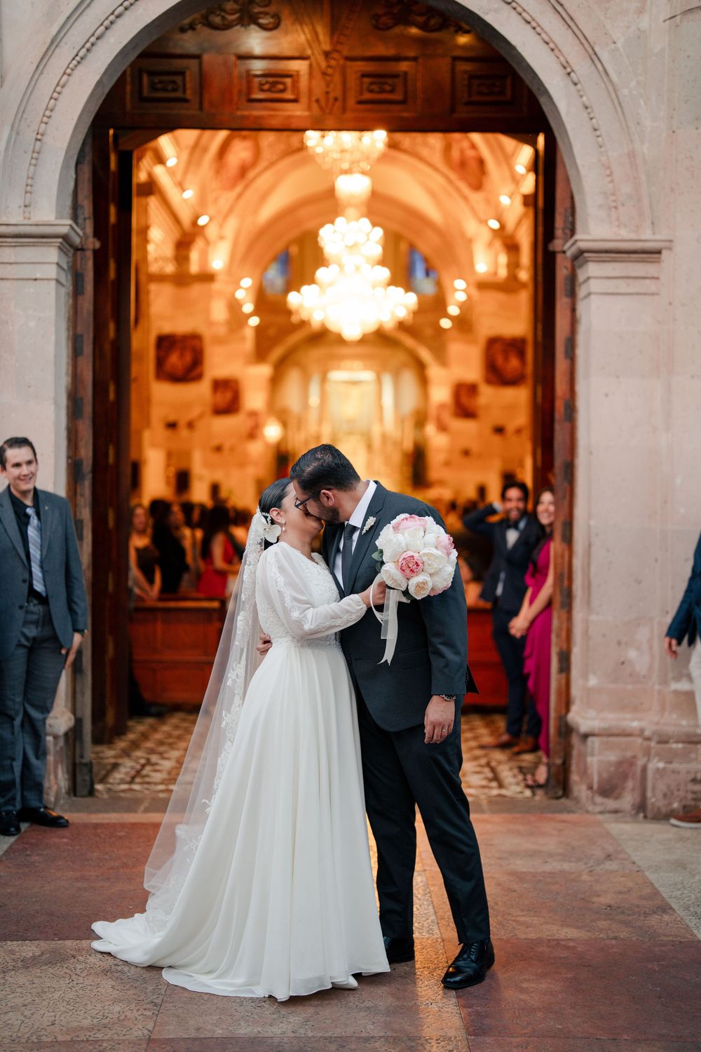 Wedding scene under ornate stone archways with warm chandelier lighting.
